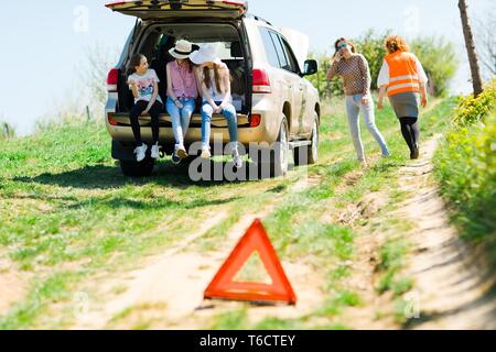 A breakdown triangle stands near a broken car - of road - family behind looking for help Stock Photo