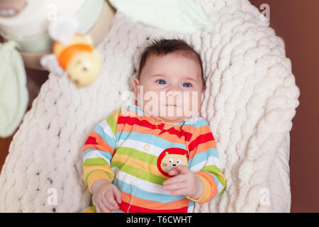 Cute adorable smiling white Caucasian baby boy girl lying in bouncer chair. Awake aware newborn infant child watching small rotating toys on babygear  Stock Photo