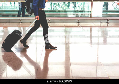 Traveler pulling suitcase in modern airport terminal. Travel and transportation concept Stock Photo