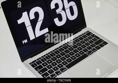 Apple MacBook Pro notebook with the clock screensaver on the big white Ikea desk office with the black yellow speakers, iPhone in the background Stock Photo