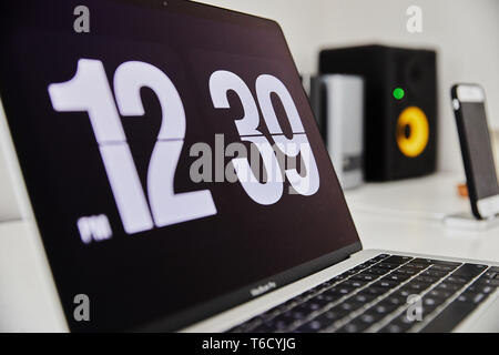 Apple MacBook Pro notebook with the clock screensaver on the big white Ikea desk office with the black yellow speakers, iPhone in the background Stock Photo