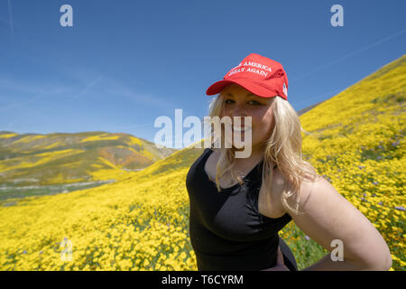 Taft, California - March 25, 2019: Blonde republican woman wears a Donald Trump Make America Great Again hat, standing in a field of yellow wildflower Stock Photo