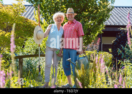 Portrait of an active senior couple holding gardening tools in the garden Stock Photo