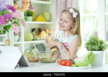 Cute little girl spicing salad on kitchen table Stock Photo