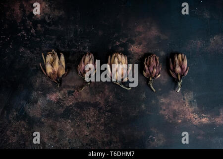 High angle close up of five baked artichokes on black rusty surface. Stock Photo
