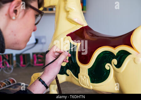 Close up of woman in workshop, painting traditional wooden carousel horse from merry-go-round. Stock Photo