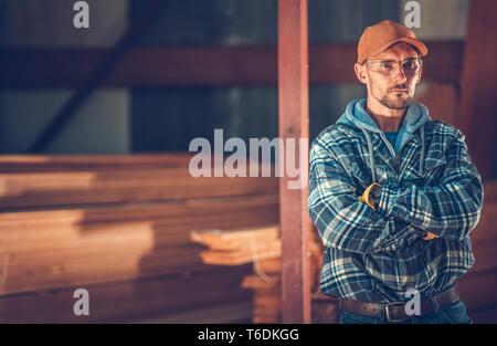 Construction Contractor Portrait. Caucasian Men Wearing Safety Glasses and Pile of Building Wood in the Background. Industrial Theme. Stock Photo