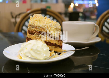 Plate of banoffee pie cake and whipped cream with blurry coffee cup in background Stock Photo