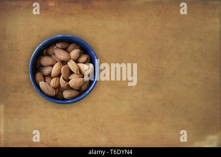 Almonds lying in a blue bowl with brown grunge background. Top view image with blank copy space for text Stock Photo