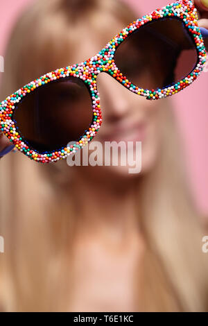 Female portrait with shallow depth of focus. Young blonde smiling  woman with fun candy glasses in hands Stock Photo