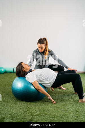 Pregnant woman doing fitness ball and pilates exercise with coach. Happy future mother preparing for childbirth. Stock Photo