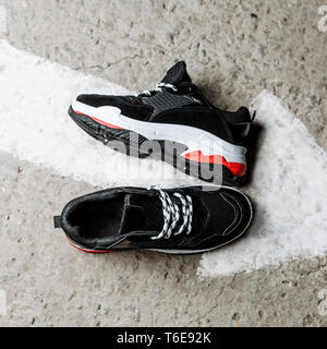 black sneakers with white laces on a thick white sole with red accents on a concrete background near a painted white arrow Stock Photo