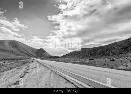 Roadside pull out looking at County road leading into mountains under sky with white fluffy clouds. Black and white. Stock Photo