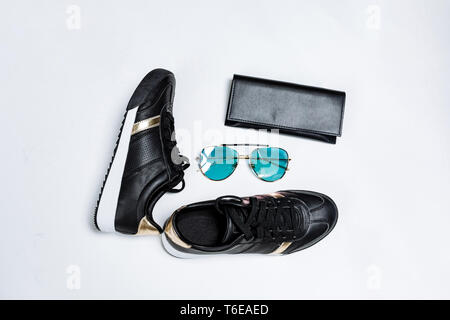 fashionable black sneakers on a white sole with black socks and gold accents, sunglasses with blue glasses and a black purse on a white background Stock Photo