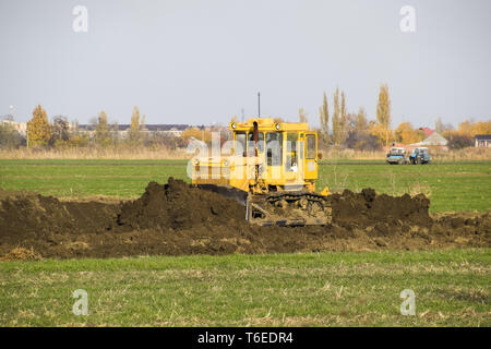 The yellow tractor with attached grederom makes ground leveling. Stock Photo