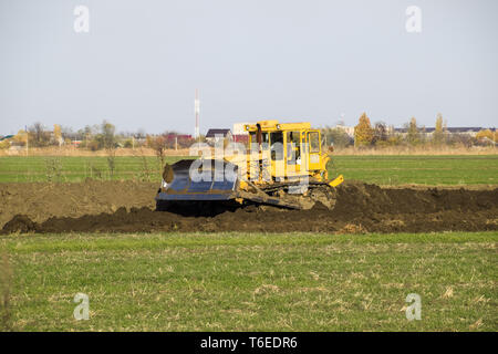 The yellow tractor with attached grederom makes ground leveling. Stock Photo