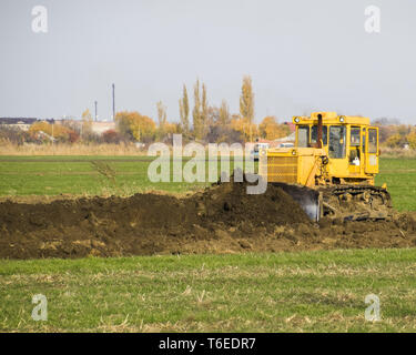 The yellow tractor with attached grederom makes ground leveling. Stock Photo