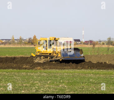 The yellow tractor with attached grederom makes ground leveling. Stock Photo