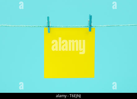 Yellow empty paper sheet on the string with clothespins over blue background Stock Photo