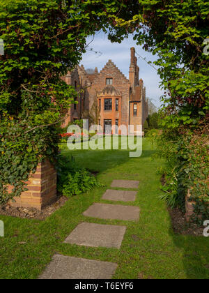 Portrait Keyhole view of path through the Akebia Quinata vine looking at  Chenies Manor House and lawn in April showing colourful tulip borders. Stock Photo