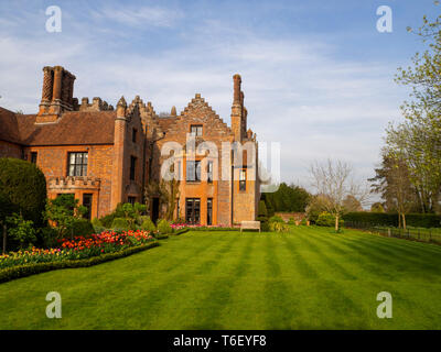 Chenies Manor House and Gardens in sunny April, showing orange colour schemed tulip borders, well maintained lawn, clipped hedges under a blue sky. Stock Photo