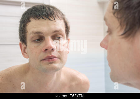 A clean-shaven young man looks in the mirror Stock Photo