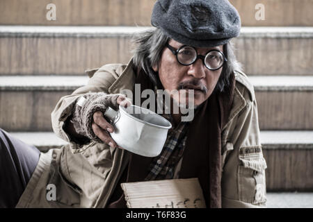 Man in need. Unhappy homeless man is holding hands to get help. Homeless. In the hands of one man metal bowl. In the hands of black gloves. Stock Photo