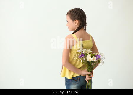 Cute little girl with bouquet of flowers on light background Stock Photo