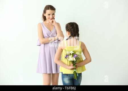 Little girl hiding flowers for mother behind her back, on light background Stock Photo