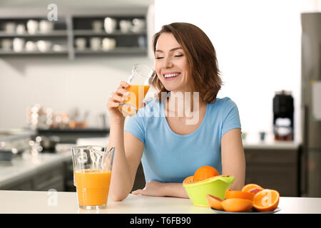 Beautiful woman drinking citrus juice in kitchen Stock Photo