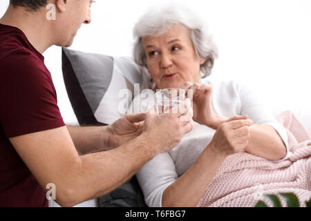 Man giving pills to elderly woman, indoors Stock Photo