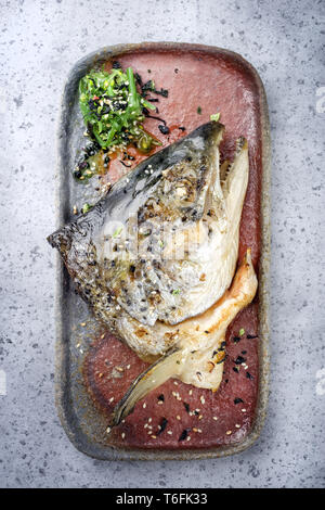 Traditional barbecue Japanese Kama Yaki broiled salmon fish head with wakame lettuce as close-up on a plate Stock Photo