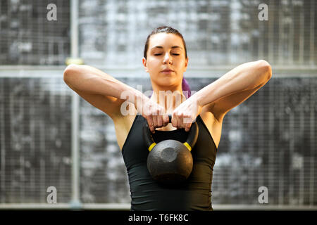 Girl working out with a kettlebell standing concentrating on her exercises with closed eyes and the weight raised in both hands to her chest inside a Stock Photo Alamy