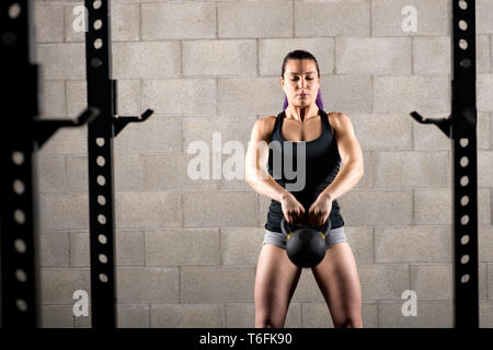 Young woman working out with a kettlebell doing a pull-up lifting the weight with both hands in front of her body to her chin in a health and fitness  Stock Photo