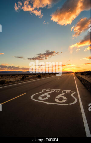 The wide open road of route 66 leading towards a dramatic sunsets over the horizon in the Mojave Dessert just outside of Amboy, California. Stock Photo