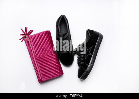 modern black suede sneakers and velvet purple clutch over a white background Stock Photo