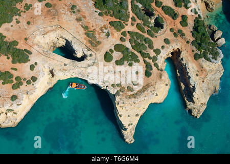 AERIAL VIEW. Sightseeing boat approaching a sea cave / sinkhole on the rocky coastline near Albandeira. Lagoa, Algarve, Portugal. Stock Photo