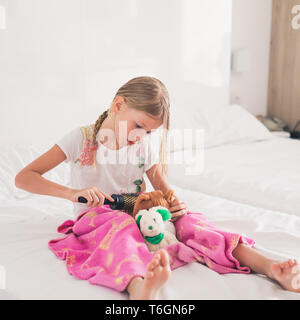 Young girl combing hair of cuddly toy Stock Photo