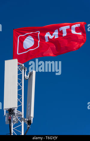 Flag with symbols of MTS (Mobile TeleSystems) - mobile operator in Russian Federation, CIS. Flag on communications tower waving in wind Stock Photo