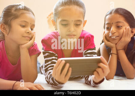 Three cute Indian children watching child using smartphone with smiley faces on bed. Stock Photo