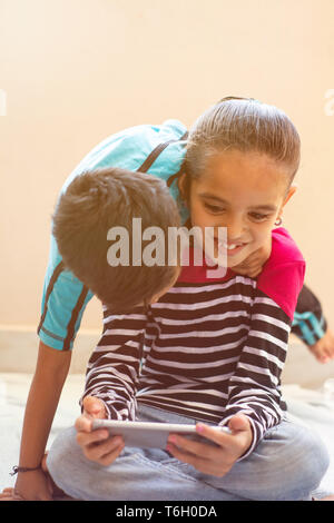 Two cute little Indian kids having fun by watching mobie device at home Stock Photo