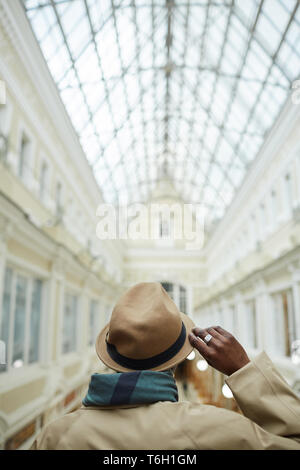 Back view portrait of trendy African man wearing hat standing in architectural building with glass roof, copy space Stock Photo