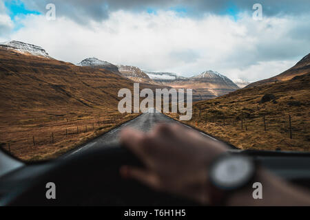 Driver's perspective from the inside of a car during a road trip through snow-covered valleys on the Faroe Islands with scenic views (Faroe Islands)