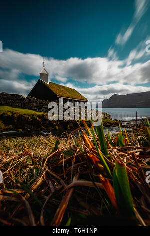 Long exposure of the small picturesque black wooden church of Funningur (Funnings Kirkja) with dramatic clouds and sun (Faroe Islands, Denmark) Stock Photo