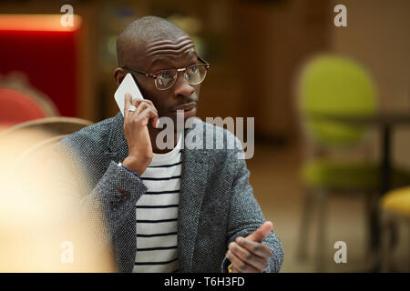 Portrait of successful African-American businessman sitting at table and speaking by smartphone, copy space Stock Photo