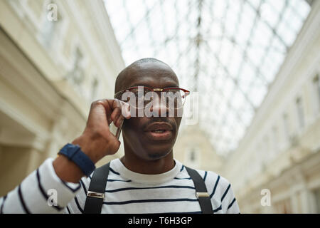 Head and shoulders portrait of contemporary African man speaking by phone standing in large architectural building, copy space Stock Photo