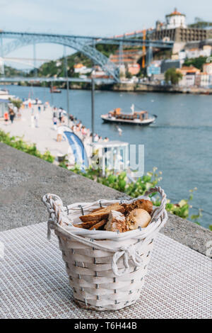 Selective focus of rustic basket full of different types of bread overlooking Cais da Ribeira and Ponte de Dom Luis I on the River Douro in Porto Stock Photo