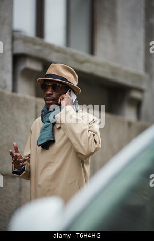 Portrait of modern African-American man wearing trenchcoat speaking by phone while walking outdoors in city, copy space Stock Photo