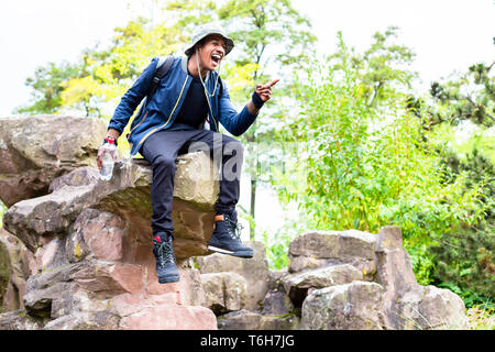 Young boy sitting on rock pointing finger laughing Stock Photo