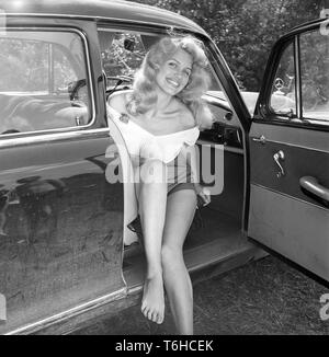 1950s summer. A young blonde woman with a big smile on her face, dressed in shorts and a jumper is sitting in a car. Photo Kristoffersson ref BX105-9. Sweden 1956 Stock Photo